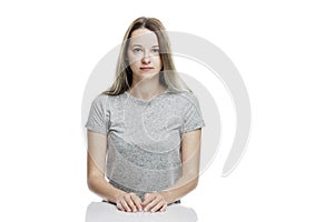 Serious young woman in a gray t-shirt is sitting at the table. Isolated on a white background