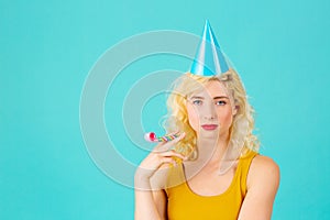 Serious young woman holding party blower with party har and looking at camera thinking