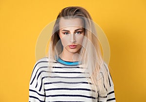 Serious young woman looking at camera, isolated on yellow background. Front view portrait of a beautiful girl