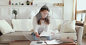 Serious young woman reviewing paperwork calculating bills at home