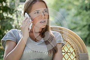Serious young woman using cell phone on chair in park