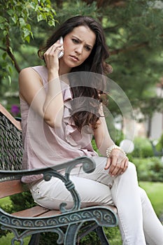Serious young woman using cell phone on park bench