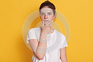 Serious young woman wearing white t shirt looking at camera with confident expression, looks thoughtful, thinks about solving