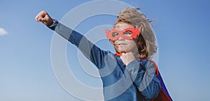 Seriuos child wearing a superhero costume. Super hero child against blue summer sky background. Kid having fun outdoors