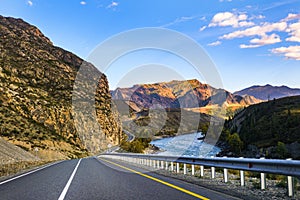 Serpentine asphalt road among high snow-capped mountain peaks, yellow desert, autumn green forest and blue sky. Car on