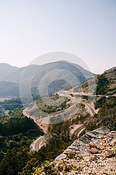 A serpentine mountain road on a mountain wasteland with green trees below and a view of the mountains.