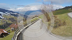 Serpentine road in high mountains, cloudy sky over green slopes, Alpine village