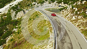 Serpentine road on highland slopes with coniferous forests. Aerial view captures red car driving along scenic freeway in