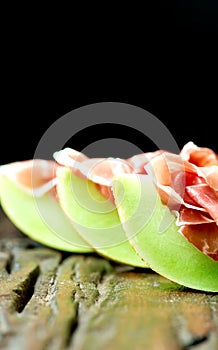 Serrano ham with melon on old wooden table on black