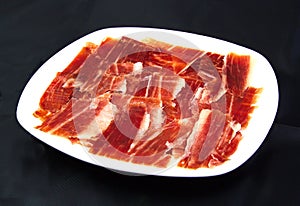 Serrano ham slices on a white dish over black