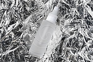 Serum with collagen and peptides on crumpled silver metal foil texture. Hyaluronic acid oil tincture on wrinkled