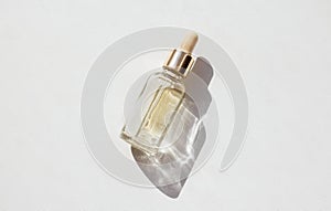 Serum with collagen and peptides in transparent glass bottle on light background with sunlight shadow