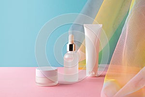 Serum, facial cleanser, moisturizer cream on blue pink background with colorful rainbow organza fishnets fabric drapery photo
