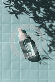 Serum glass bottle on the water texture on blue paper checkered texture background on the sunlight with leaves shadow.