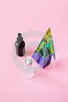Serum jars with pipette mockups and glass pyramid prism on pink background with copy space, vertical. Beauty skin care