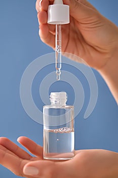 Serum with a pipette in female hands on a blue background.