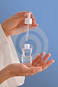 Serum with a pipette in female hands on a blue background.