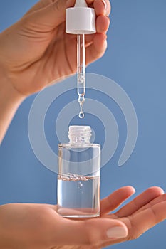 Serum with a pipette in female hands on a blue background.