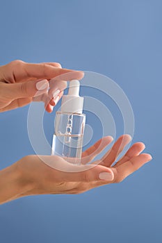 Serum with a pipette in female hands on a blue background.