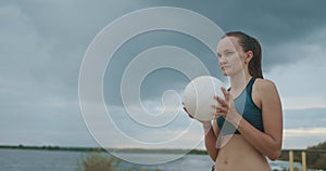 Serve in beach volleyball, young female player is holding ball in hands, throwing up and striking, medium portrait