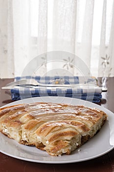 Served balkan burek cheese pie on the plate with silverware on the plate in the background