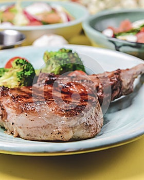 Served roast beef meat steak with brocoli cabbage and cherry toamtoes on a blue plate over bright yellow background