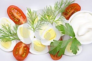 An overhead photo of vegetable salad with mayonnaise, boiled quail egg, dill, fresh tomato and parsley on white porcelain plate. A