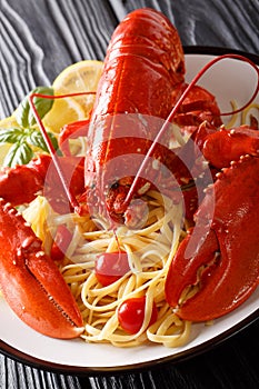 Served spaghetti pasta with red lobster, tomatoes, lemon and fresh herbs close-up on a black background. Vertical