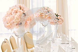 Served table for event dinner with cutlery and glasses, decorated with floral compositions in vases.