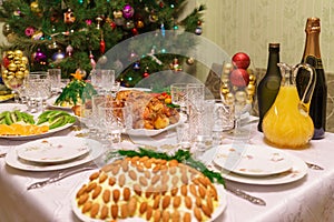Served table with festive dishes near beautiful decorated Christmas tree in living room interior. Concept of new year holiday at