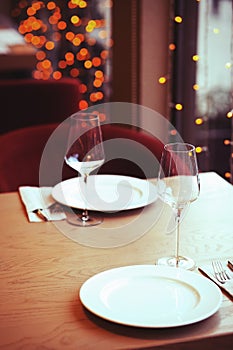 Served table in the restaurant. Empty wine glasses, a plate on the background of the bright lights of the Christmas garland