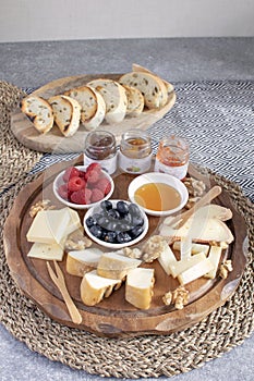 Served table - wine appetizer, cheese assortment on round wooden board, walnuts, berries, honey, jams, bread, copy space