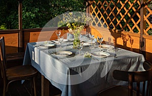Served table at wooden summer terrace. Country house in Russia. Everning meal. Glasses and wild flower