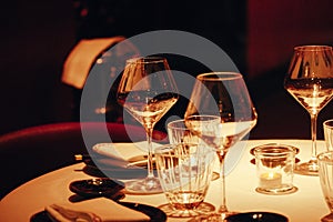 Served tables with white tablecloths with plates, glasses, white napkins inside a luxury restaurant in the evening dark