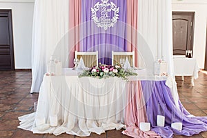 Served wedding banquet table in the restaurant decorated white, pink and purple material, white and pink flowers and greenery.