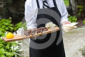 A server holding a wooden tray full of meat snacks during a catered event