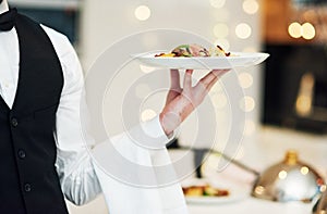 He serves with class. an unrecognizable young waiter holding a plate of food in a restaurant.