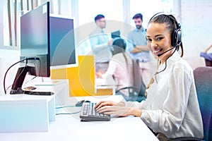 IT service desk operator woman in headset working on computer and posing to camera.