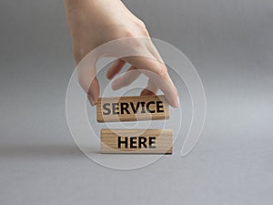 Service here symbol. Concept words Service here on wooden blocks. Beautiful grey background. Businessman hand. Business and