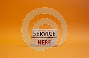 Service here symbol. Concept words Service here on wooden blocks. Beautiful orange background. Business and Service here concept.