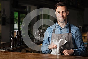 Service at pub. Barman wipes empty glass, standing at bar in interior