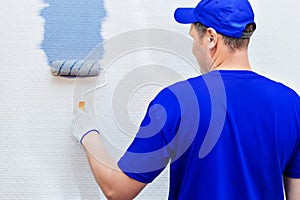 Service Repair and restoration of premises. Portrait of a house painter and a paint roller painting the wall in blue.