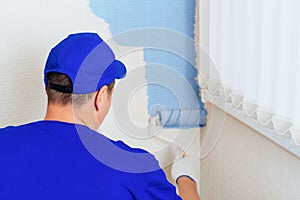 Service Repair and restoration of premises. Portrait of a house painter and a paint roller painting the wall in blue.