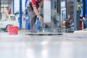 Service staff man using a mop to remove water in the uniform cleaning the protective clothing of the new epoxy floor in an empty