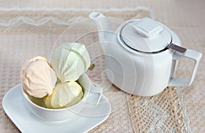 On a serviced table with a beige tablecloth lies a stunning fresh marshmallow and a teapot with fragrant tea