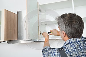 Serviceman Fixing Cabinet With Screwdriver In Kitchen photo