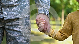 Serviceman holding boys hand, army defending safe future, family togetherness