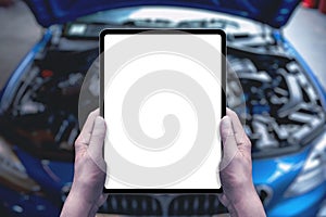 Serviceman holds a tablet in front of a car with an open engine compartment