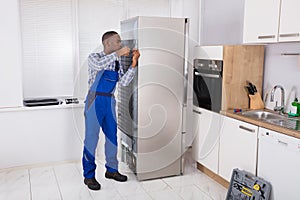 Serviceman In Overall Working On Fridge