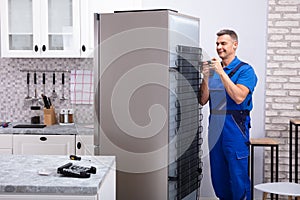 Serviceman In Overall Working On Fridge photo